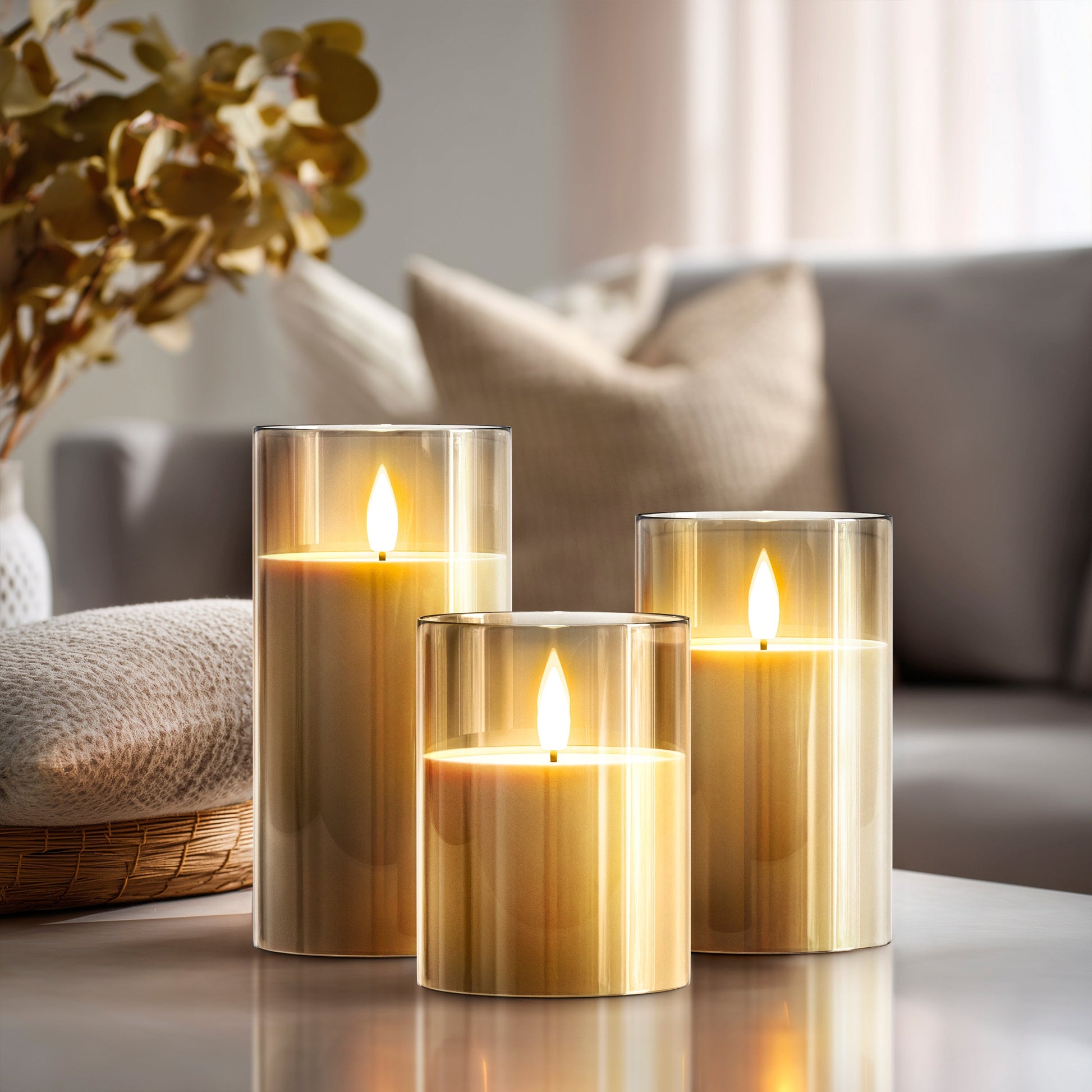 Three lit candles in glass holders on a table with a blurred background of a living room.