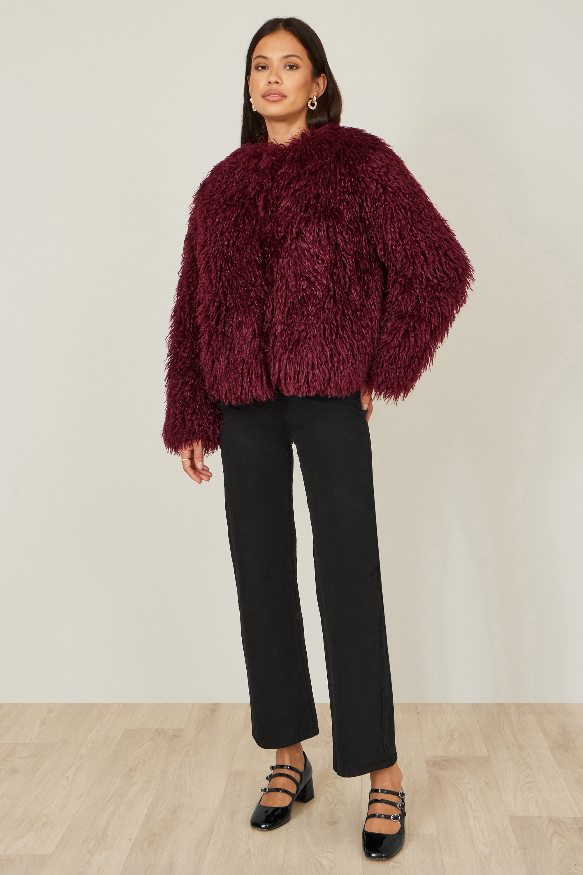 Close up of burgundy fluffy faux fur coat showing soft plush texture and rich colour