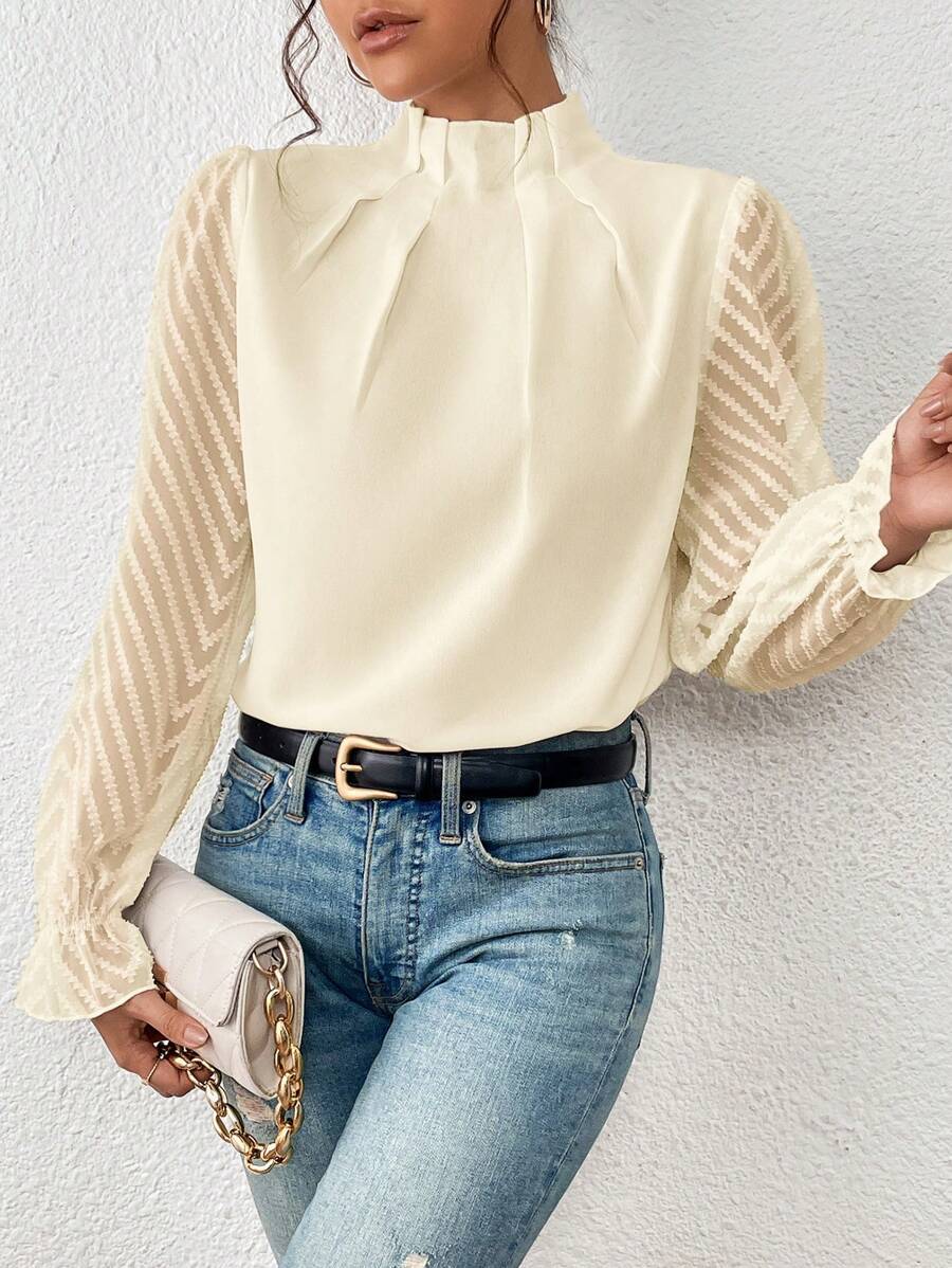 Woman wearing a beige blouse with long sleeves and blue jeans against a white background