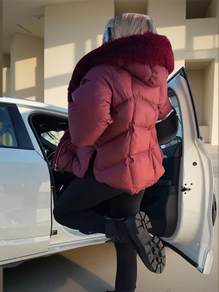 Person in a red puffer jacket with a fur-lined hood getting into a white car.