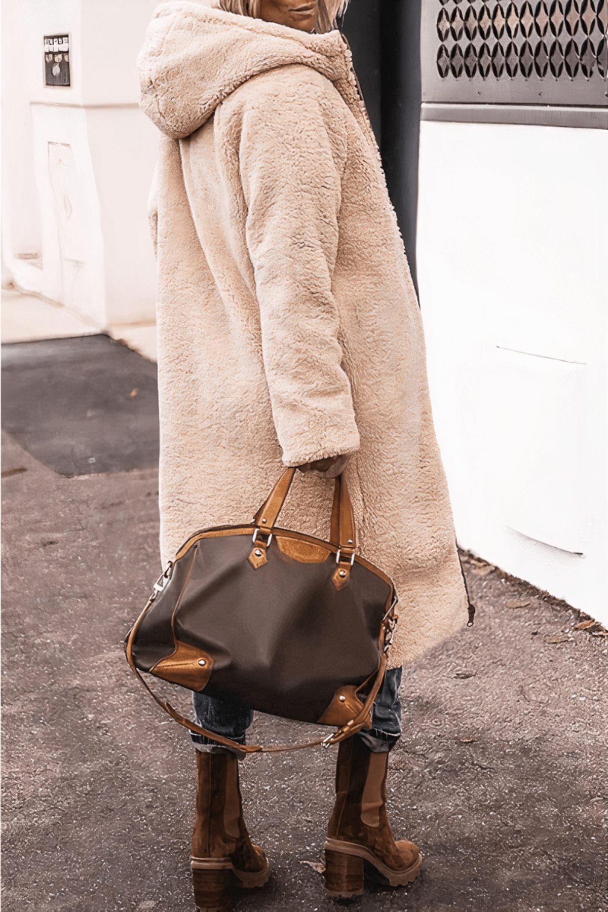 Person wearing a reversible jacket outside blue and reversible beige fleece-lined coat holding a brown handbag on a street.